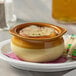 An Acopa brown and ivory stoneware onion soup bowl on a plate with soup