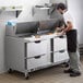 A man in a white shirt and black apron is using a Beverage-Air Elite Series Mega Top Sandwich Prep Table to prepare food.