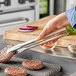 A person using Vollrath stainless steel tongs to cut up burgers.