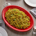 A Tuxton cayenne oval china platter holding pasta with basil on a table with a glass of wine.