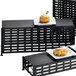 A black rectangular lattice riser with food on a table.