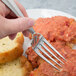 A hand holding a Bon Chef Monroe stainless steel dinner fork over a plate of food.