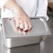 A person wearing plastic gloves holding a Vollrath stainless steel hotel pan cover.