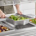 A person preparing a salad in a Vollrath stainless steel hexagon pan on a counter.