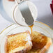 A person using a Tablecraft white dispenser to pour syrup on a piece of toast.