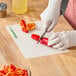 A flexible cutting board mat with a logo being used to slice bell peppers on a wooden countertop.