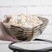 A person holding a Vollrath double wall metal serving bowl filled with potato salad.