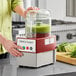 A person using a Robot Coupe food processor with a clear bowl to blend food.