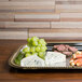 A Vollrath metal catering tray with cheese, grapes, and salami on a table.