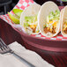 A plate of tacos in a HS Inc. raspberry round deli server with a fork and lime.