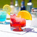 A Libbey old fashioned glass filled with a red drink and a slice of orange on a table.