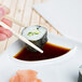 A person holding chopsticks to a sushi roll on a white CAC divided sauce plate.