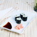 A CAC white divided sauce plate with sushi rolls and sauce.