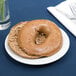 A Tuxton Alaska bright white wide rim china plate with a bagel on it.