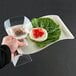 A hand holding a Fineline bone plastic cocktail plate with food and a glass of liquid.