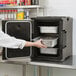 A woman in a white coat opening a black Cambro Ultra Pan Carrier in a professional kitchen.
