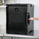 A person opening a black Cambro Ultra Pan Carrier on a counter.