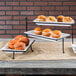 An American Metalcraft three-tier rectangular display stand with trays of muffins on a table.