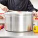 A person stirring food in a Vollrath heavy duty aluminum sauce pot.