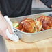 A person using a Vollrath aluminum baking and roasting pan to prepare food.