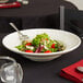 A salad with tomatoes and chicken in a white Tuxton pasta/salad bowl on a table.