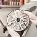 A person in gloves holding a Hobart fine cheese grater plate, a circular metal object with holes in it.