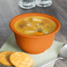 A Fiesta Tangerine china bouillon filled with soup and a cracker on a napkin.