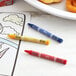 A yellow cellophane-wrapped package of Choice Kids' Restaurant Crayons on a table with a plate of food and a donut.