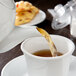 A cup of tea being poured into a white CAC porcelain teapot.