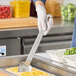 A person in a white apron using a Vollrath stainless spoon to scoop food.