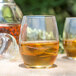 Two Chef & Sommelier old fashioned glasses filled with brown liquid and ice sit on a table.