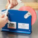 A hand using a blue Shurtape dispenser to seal a plastic bag.