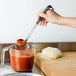 A person using a Vollrath Jacob's Pride ladle with a black handle to pour sauce into a measuring cup.