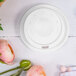 A white plastic Dart travel lid with a lid on top next to pink flowers.