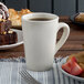 A white Tuxton china mug filled with brown liquid on a table with desserts.