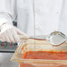 A person in white gloves using a Vollrath ivory Spoodle to serve red sauce from a glass container.