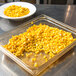 A Carlisle amber food pan drain tray on a counter with a bowl of corn.