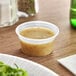 A clear plastic Dart souffle container filled with sauce on a table.