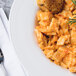 A white porcelain pasta bowl filled with pasta and a piece of bread on a table.