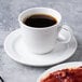 A plate with a piece of strawberry pie and a white porcelain tea cup on a saucer with coffee.