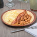 A Libbey mustard yellow terracotta plate with bacon, eggs, and potatoes on it on a table.
