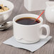 A close-up of a Libbey ivory porcelain large stacking cup of coffee with a spoon.