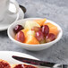 A white Aluma porcelain bowl filled with grapes, apricots, and other fruit.