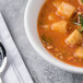 A white Libbey Aluma porcelain bowl of soup with vegetables and herbs.