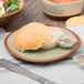 A Libbey fern green terracotta plate with food and a bread roll on a table.