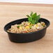 A Pactiv black plastic VERSAtainer oval microwavable container with rice and vegetables.