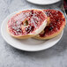 A Libbey white porcelain plate with a bagel and sandwich with jam on it.