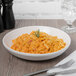 A Libbey ivory porcelain shallow pasta bowl filled with pasta and a sprig of rosemary with silver utensils on a white napkin.