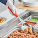 A person holding a Vollrath orange solid oval spoodle over a bowl of meatballs.