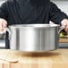 A person in a black coat holding a large silver Vollrath Tribute brazier.